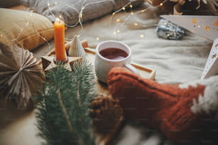 Xícara de chá quente, meias de lã, estrelas de Natal, luzes douradas, árvores, velas e travesseiros na cama macia. Momentos aconchegantes em casa escandinava. Férias de inverno e outono. Conforto e relaxamento