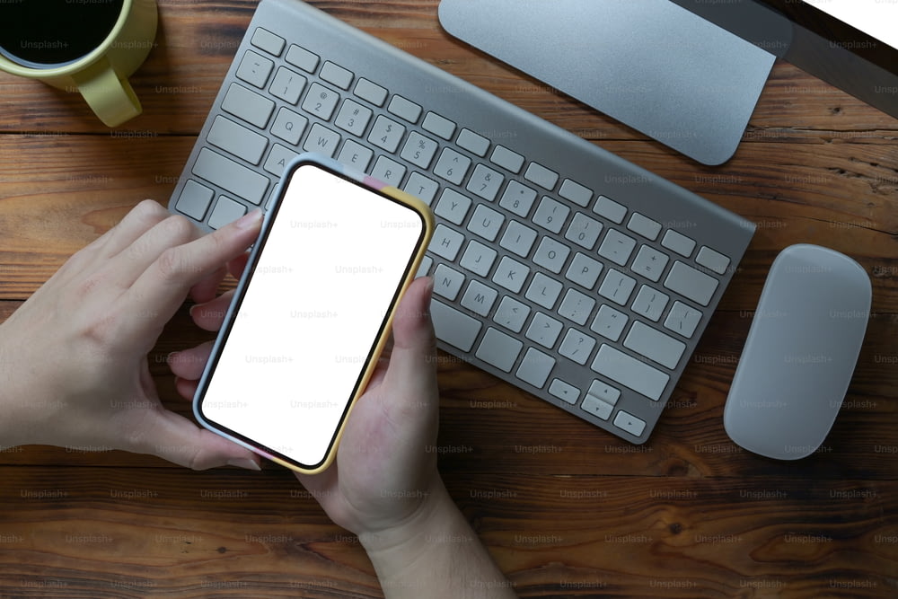 Mains d’homme tenant un téléphone intelligent avec écran blanc sur une table en bois.