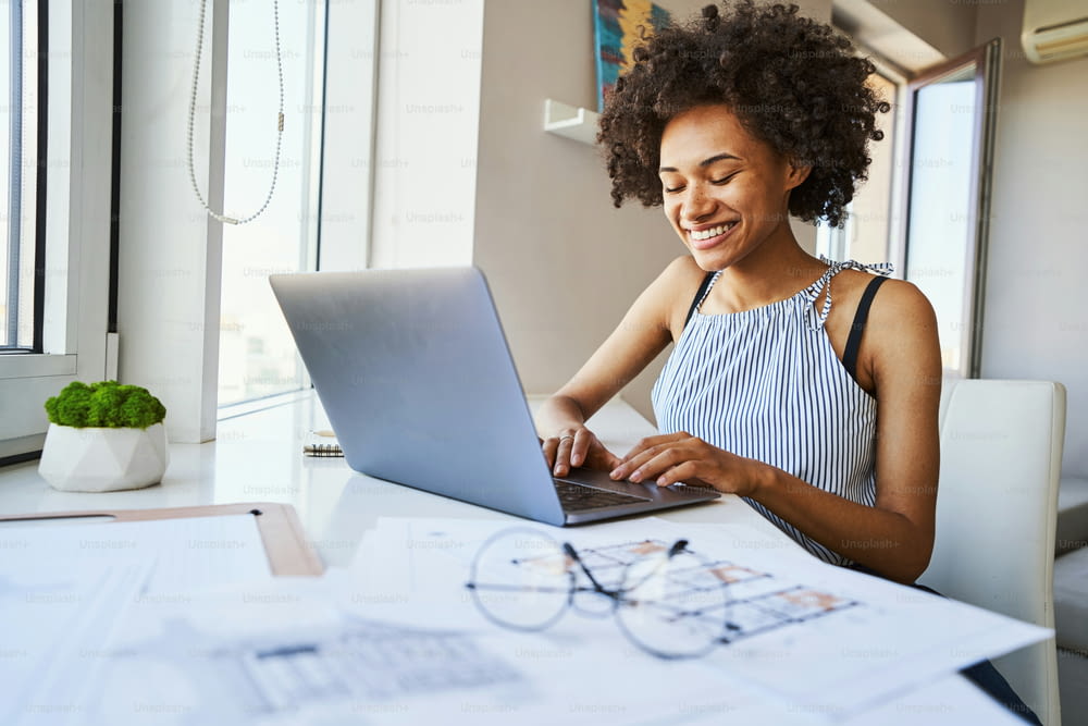 Smiling joyous attractive young African American female architect replying to an email in the morning
