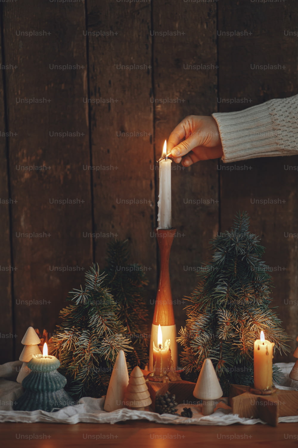 Adviento festivo. Mano en suéter acogedor que enciende la vela de Navidad sobre fondo de madera rústica con pinos y conos en la habitación escandinava de la noche.  Momento atmosférico