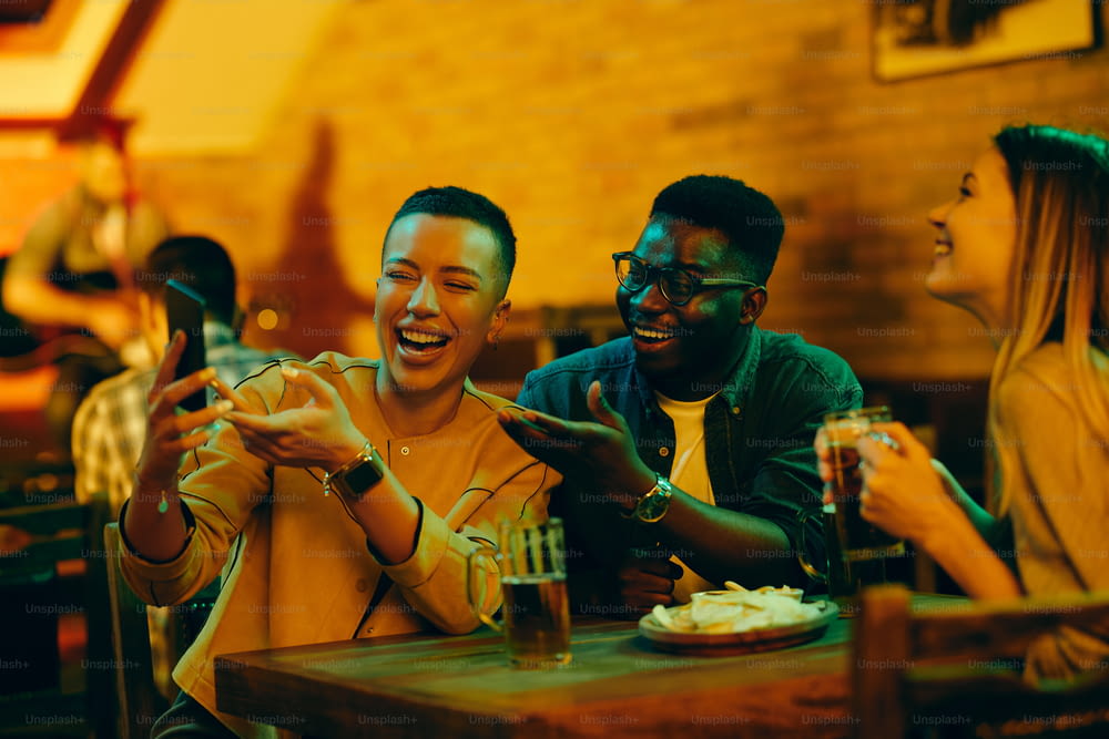 Gruppe glücklicher Freunde, die Spaß beim Biertrinken und Handy in einer Bar haben.