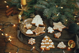 Christmas gingerbread cookies, fir branches, warm lights on napkin and rustic wooden table. Moody atmospheric image. Winter countryside hygge. Happy Holidays and Seasons greeting