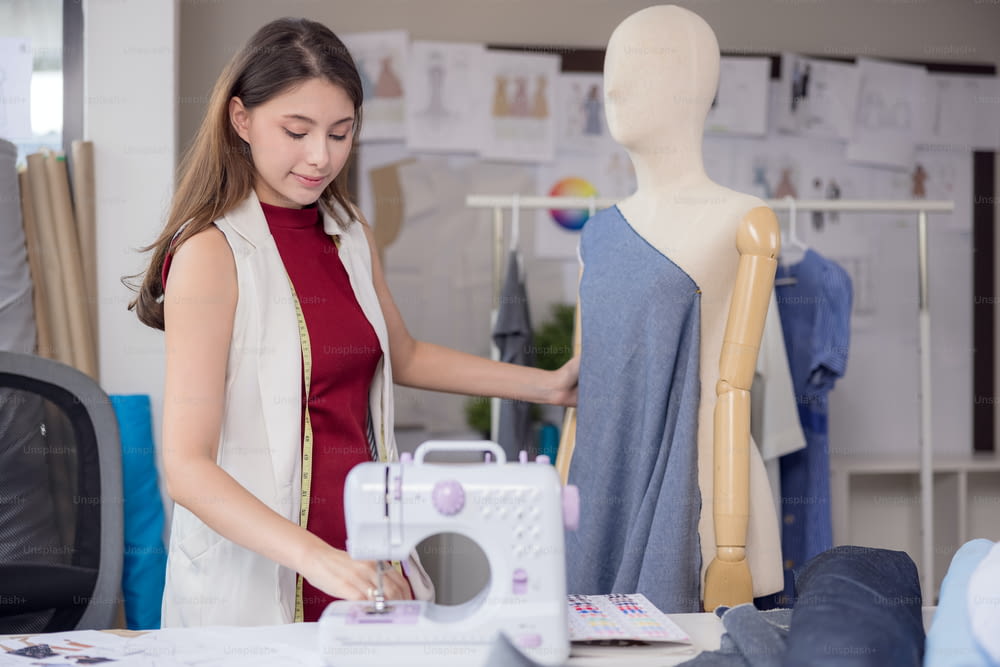 모델은 패션 디자이너가 새로운 디자이너 의류를 입어보기 위해 사용합니다. 직장에서 직물 사업의 여성 기업가는 패션 디자이너를 위해 새로운 옷을 디자인하고 있습니다.
