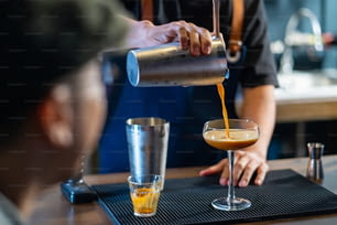 Barista asiático agitando café negro helado en una coctelera y vertiendo en una copa de cóctel en la barra del bar de la cafetería. Propietario de una cafetería que sirve café frío al cliente. Concepto de restaurante para pequeñas empresas.