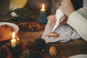진저 브레드 쿠키 크리스마스 트리를 냅킨, 양초, 향신료, 장식으로 소박한 테이블에 설탕을 입히는 손. 분위기 있는 분위기 있는 이미지. 전통적인 크리스마스 진저 브레드 쿠키 만들기