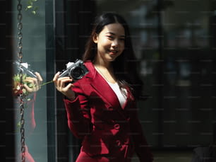 Young asian female in red suit with photo retro or vintage camera standing in the modern studio office