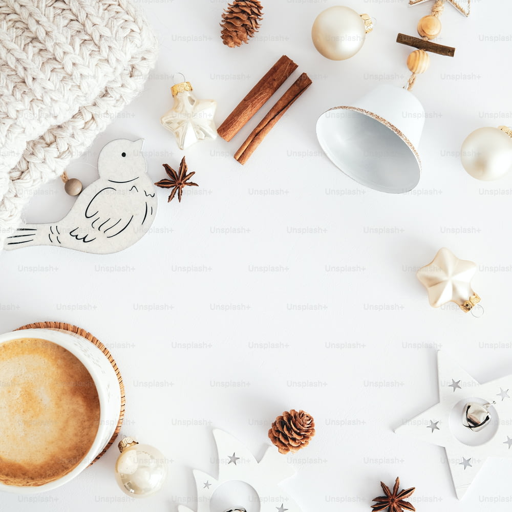 Composition de Noël. Décorations de Noël en bois de style nordique, tasse de café, bâtons de cannelle, cloches, boules beiges sur une table blanche. Hygge, décoration d’intérieur bohème.