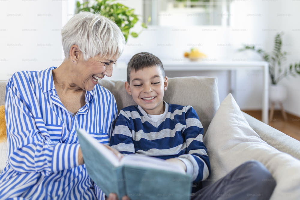 室内で孫と一緒に本を見ている幸せな白髪の女性のトリミングされた写真。彼らは会話中に笑顔を浮かべています。祖父母訪問のコンセプト