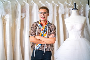 ウェディングスタジオの試着室でマネキンを縫う上でウェディングドレスを測定する巻尺を使用するアジアのLGBTQの男のブライダルショップのオーナーの肖像画。中小企業の起業家、ウェディングプランナー、テーラーデザイナーのコンセプト