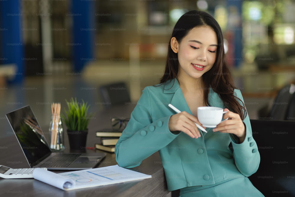 Successful asian young business woman or female manager sitting in board room and sipping hot tea or coffee.