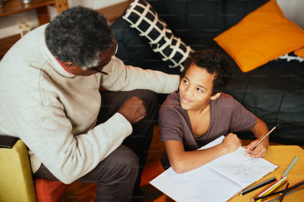 Un abuelo afroamericano está sentado en casa con su nieto y lo ayuda con la tarea.