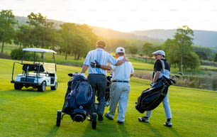 Un grupo de asiáticos, un hombre de negocios y un director ejecutivo senior disfrutan juntos del deporte al aire libre jugando al golf en un club de campo. Golfista de hombres sanos sosteniendo bolsa de golf caminando en la calle con hablando juntos en la puesta del sol de verano