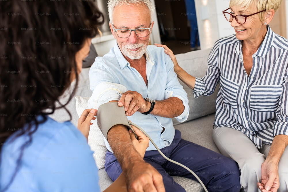Enfermeira conversando com pacientes idosos enquanto estava em uma visita domiciliar medindo a pressão arterial.