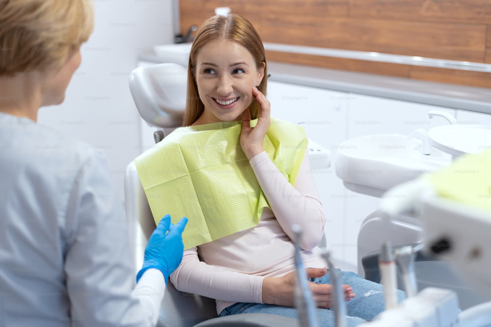 Portrait d’une jeune femme souriante se sentant heureuse après le traitement des dents. Consultation avec un densististe professionnel. Cabinet de la clinique de stomatologie moderne. Industrie de la médecine buccale