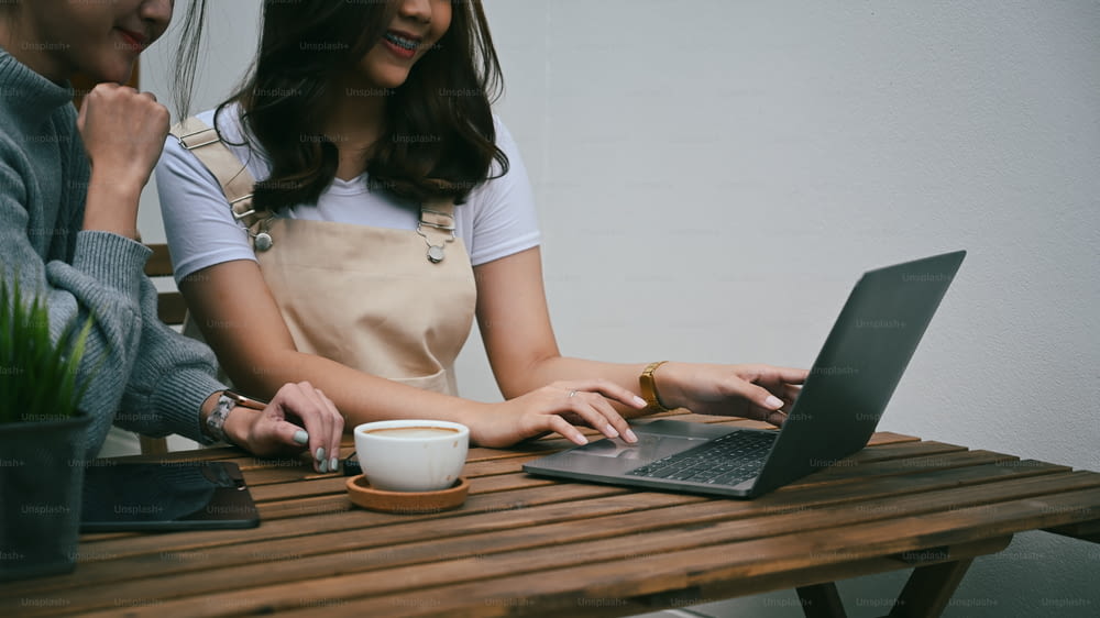 屋外のカフェに座っている間、ラップトップコンピュータを使用している2人の若いアジア人女性。