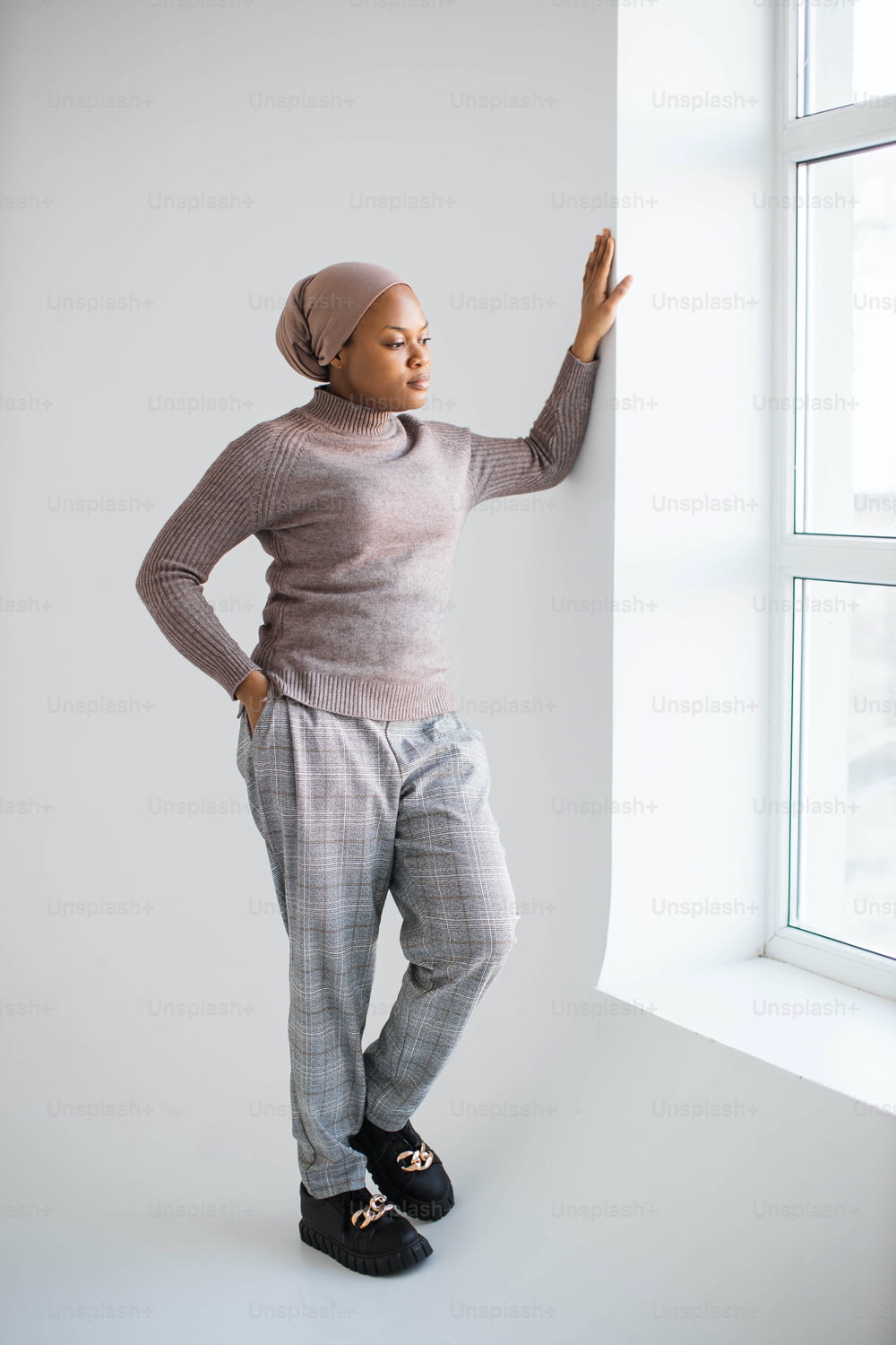 白い背景のスタジオに立って窓を見ているスカーフとカジュアルな服を着た魅力的なアフリカ系アメリカ人のイスラム教徒の女性。人とライフスタイルのコンセプト。
