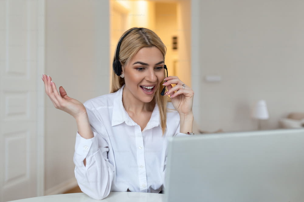 Happy blond woman wearing headphones and microphone looking at webcam, smiling at camera, laughing during virtual meeting or video call talk. Employee working from home. Screen view head shot