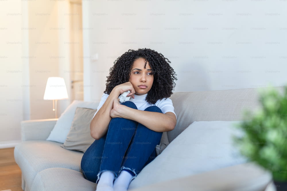 젊은 아프리카계 미국인 여성은 화가 나거나, 슬프거나, 불행하거나, 실망스러워하며 방에서 외롭게 울고 있습니다. 우울증으로 고통받는 여자 침대에 앉아 울고 있다