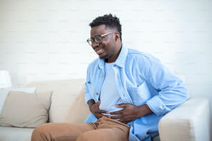 Young African man holding his stomach in pain, Man with reflux disease holding his belly with painful expression