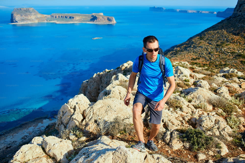 Il viaggiatore maschio con lo zaino corre sulla scogliera contro il mare e il cielo blu al mattino presto. spiaggia di Balos sullo sfondo, Creta, Grecia