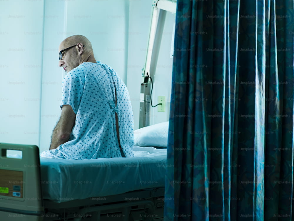 Un uomo in camice d'ospedale seduto su un letto d'ospedale