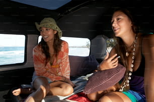 Zwei junge Frauen sitzen auf der Ladefläche eines Lieferwagens