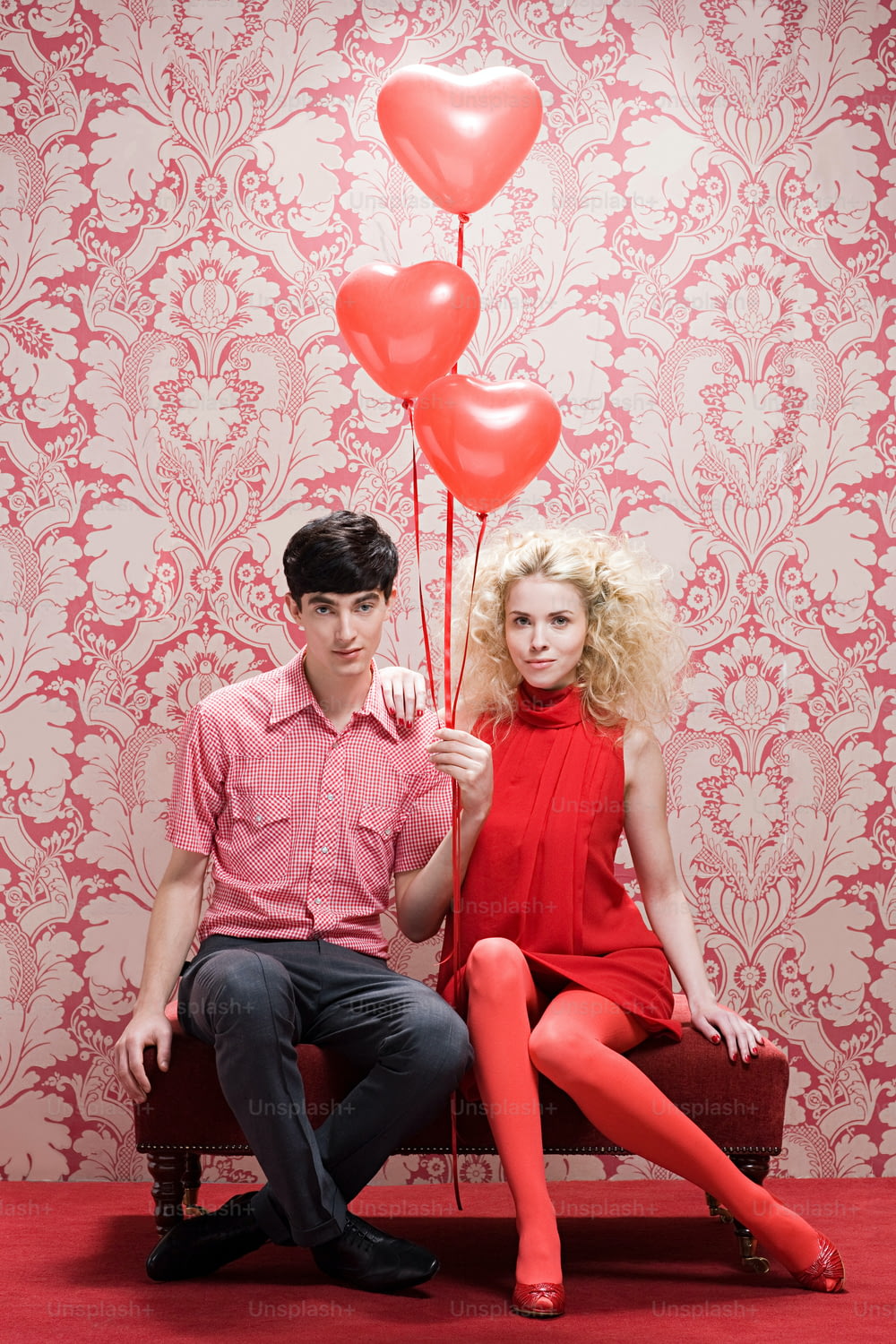 a man and a woman sitting on a bench with red balloons