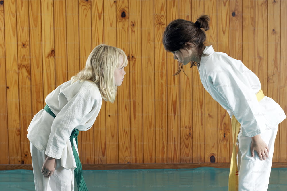 Due ragazze in uniformi di karate in piedi davanti a una parete di legno