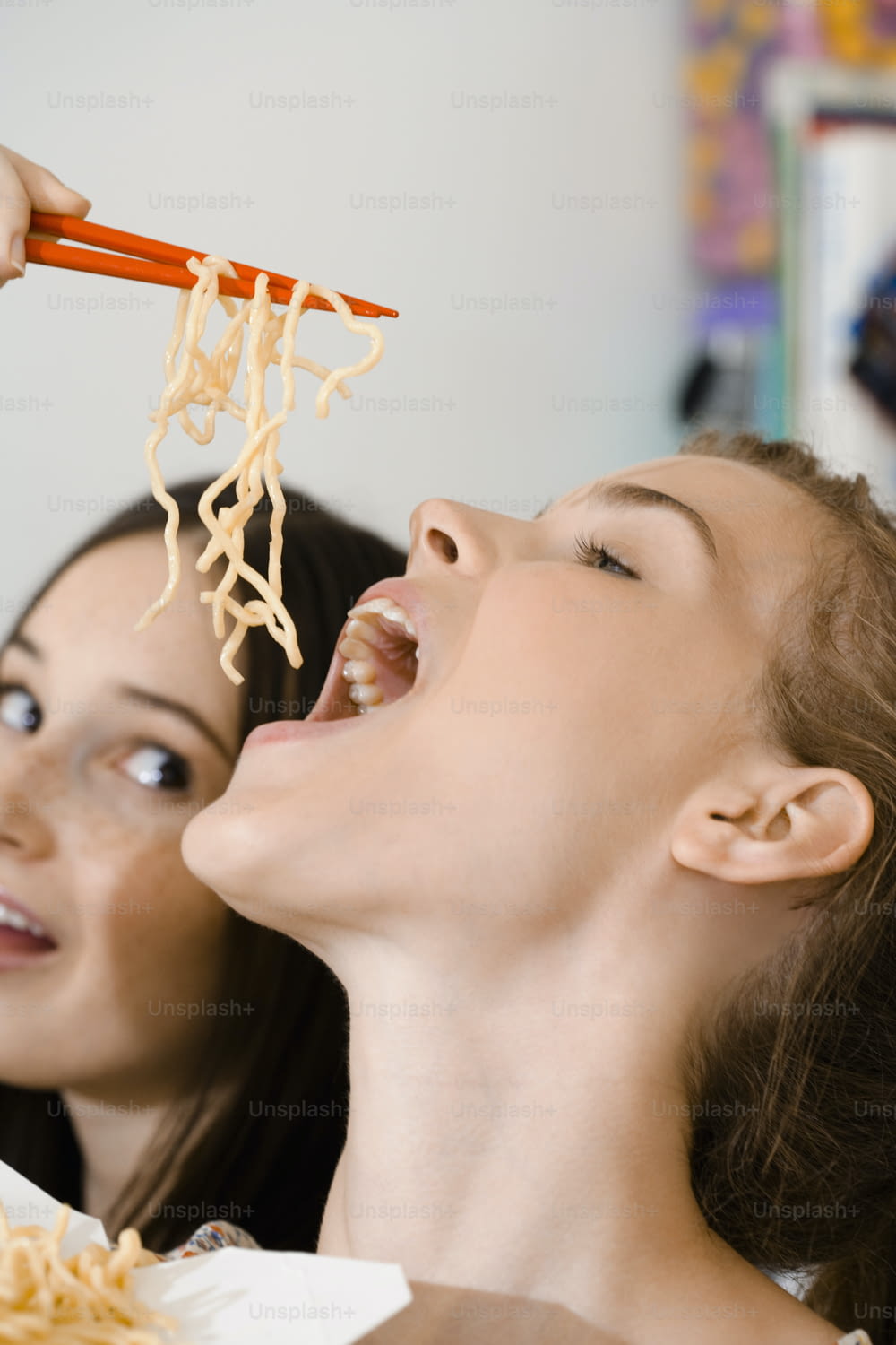 Una donna che mangia noodles con le bacchette mentre un'altra donna guarda