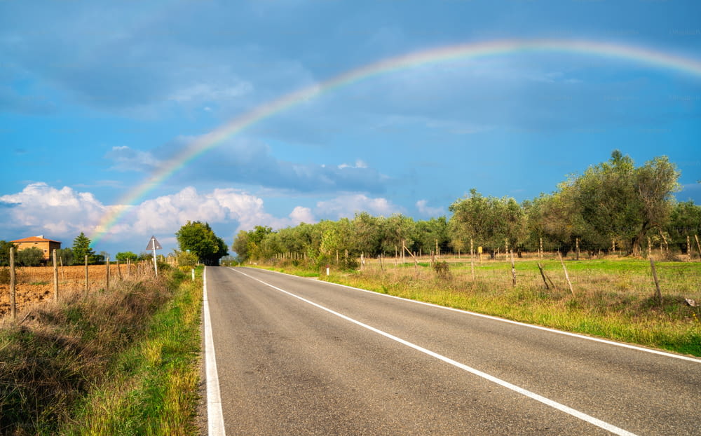 Arco-íris sobre a estrada da estrada rural e a paisagem agrícola na Toscana, Itália.