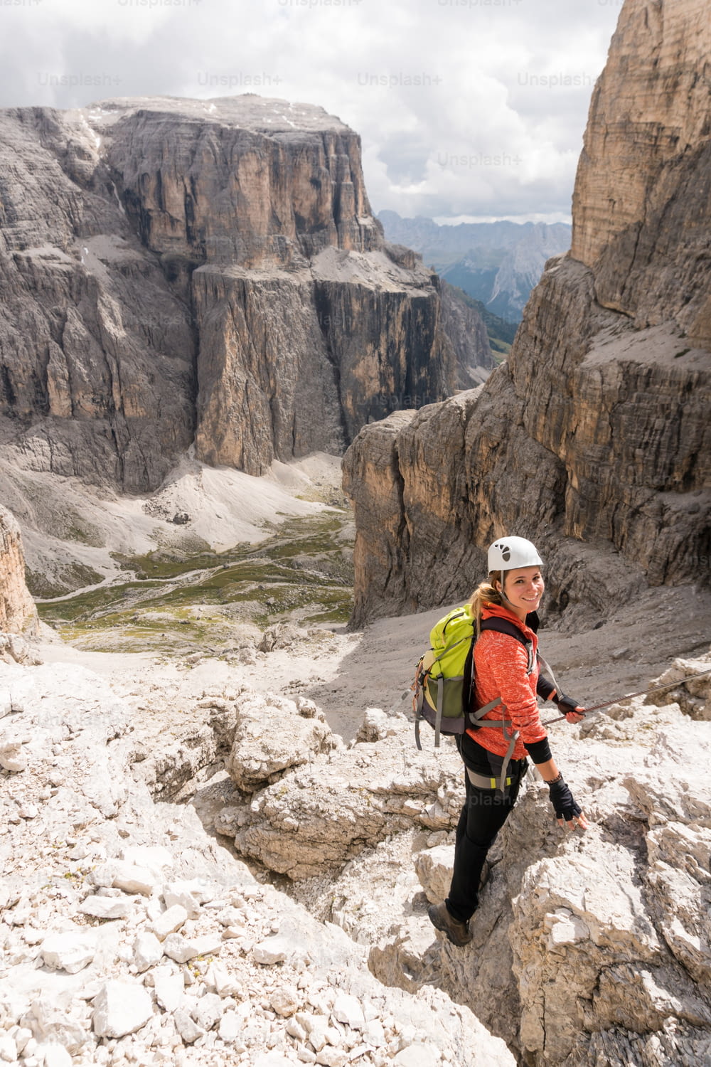 young female mountain climber descending a steep Via Ferrata in the Dolomites of Alta Badia in northern Italy with great landscape behind