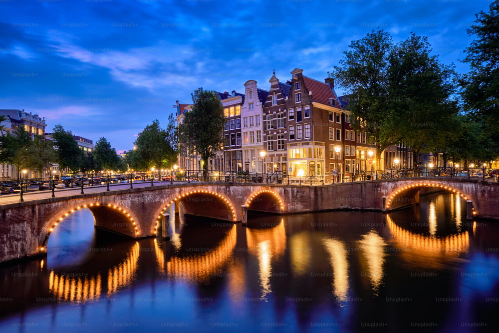 Vista nocturna del paisaje urbano de Amterdam con el canal, el puente y las casas medievales en el crepúsculo de la tarde iluminado. Ámsterdam, Países Bajos