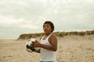 a woman holding a soccer ball on a beach