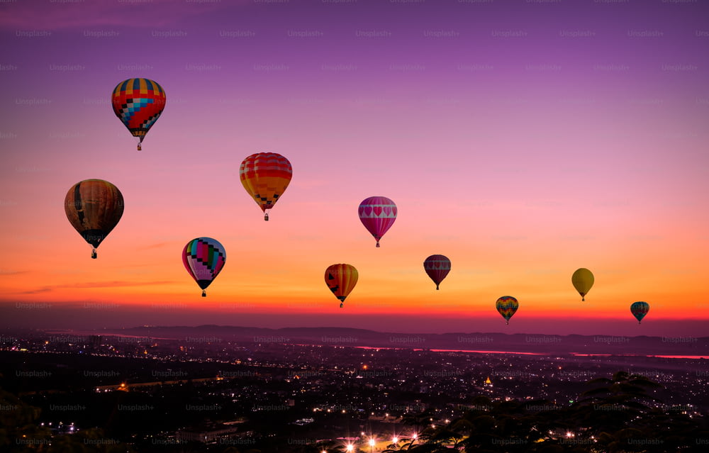 Les montgolfières colorées volant au-dessus de la ville au coucher du soleil avant la tombée de la nuit avec des couleurs de lumière et un beau fond de ciel au crépuscule et au coucher du soleil.