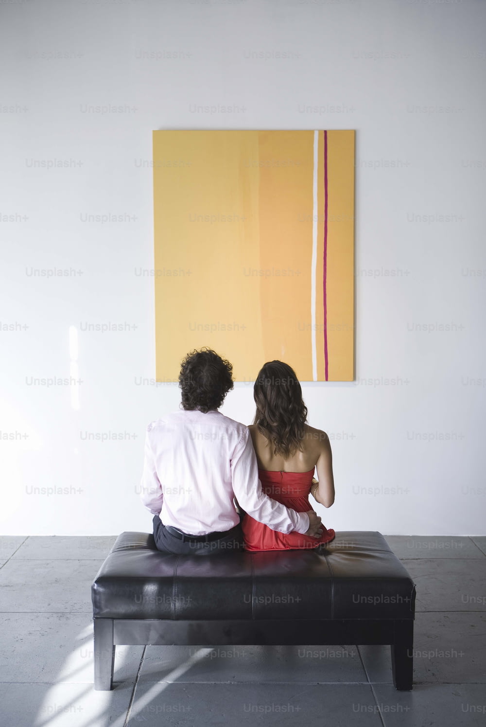 un homme et une femme assis sur un banc devant un tableau