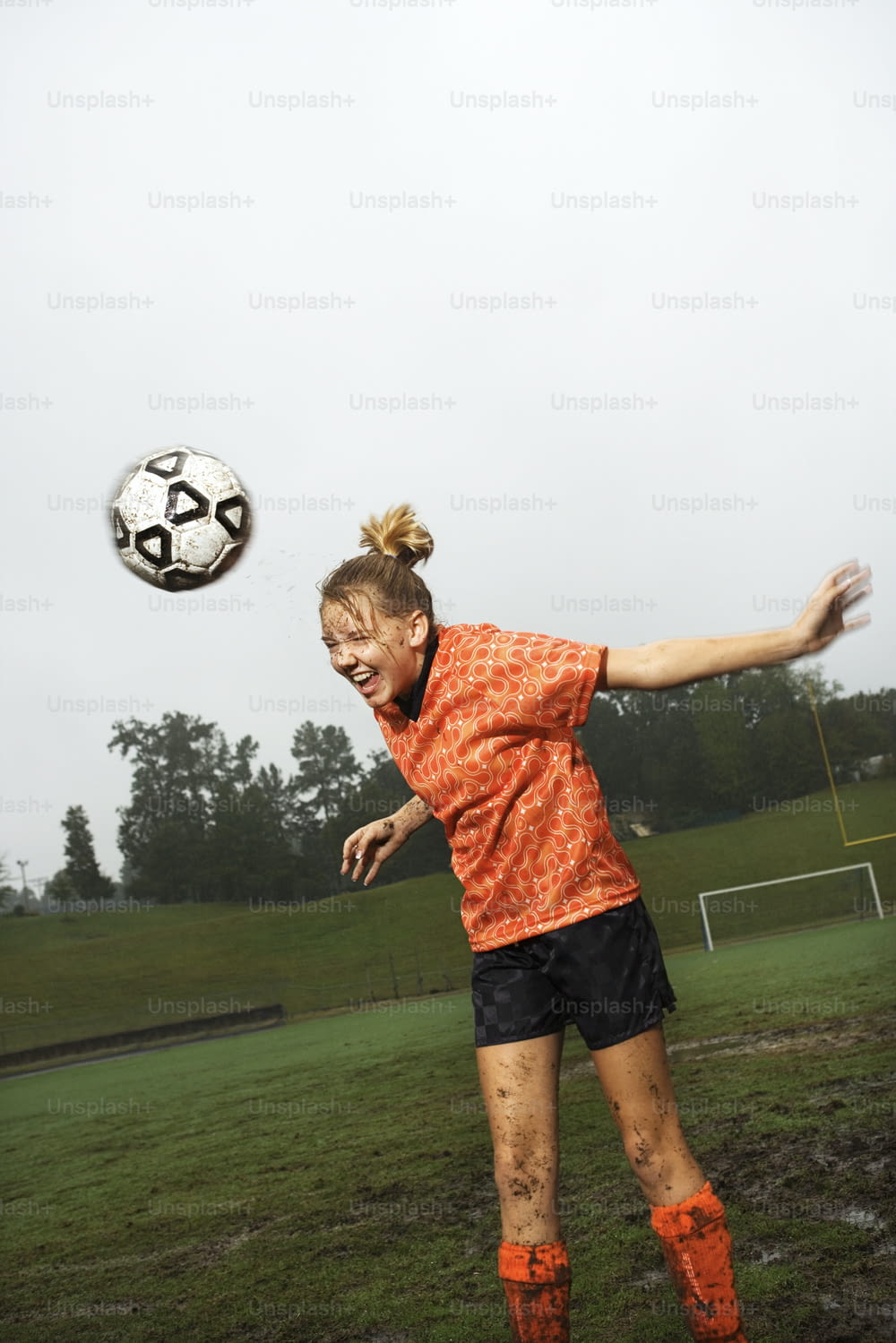 Eine Frau in einem orangefarbenen Hemd und schwarzen Shorts, die einen Fußball tritt