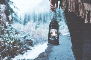 石油ランプを持って雪に覆われた森の中を旅する女性。クローズ アップ。ポンチョを着ています。冬がやってくる。放浪癖と自由奔放に生きるスタイル