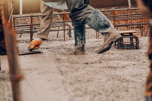 Ouvrier de chantier en bottes et uniforme de finition du béton au sol.