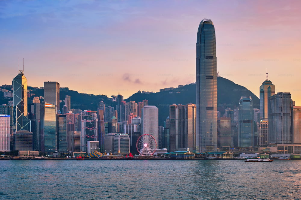 홍콩 스카이라인 도시 풍경 시내의 고층 빌딩이 저녁에는 빅토리아 항구 위로 올라가고 일몰에 정크 관광 페리 보트가 극적인 하늘을 감상할 수 있습니다. 홍콩, 중국