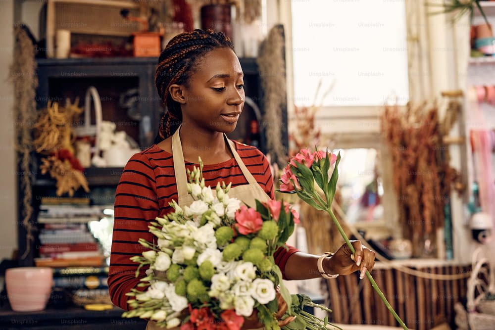 Donna afroamericana che usa fiori freschi mentre fa bouquet al lavoro in un negozio di fiori.