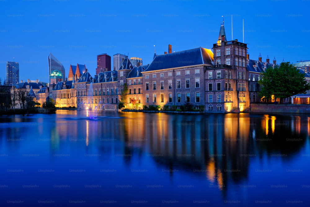 Blick auf das Parlamentsgebäude Binnenhof und den Hofvijver-See mit den Wolkenkratzern in der Innenstadt im Hintergrund, die abends beleuchtet werden. Den Haag, Niederlande
