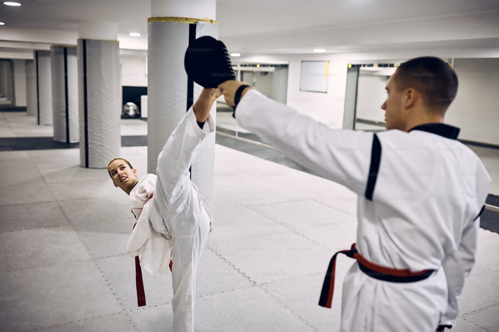 Kampfkünstlerin mit Para-Fähigkeit, die mit ihrem sparsamen Partner einen hohen Tritt übt, während sie Taekwondo im Fitnessstudio übt.