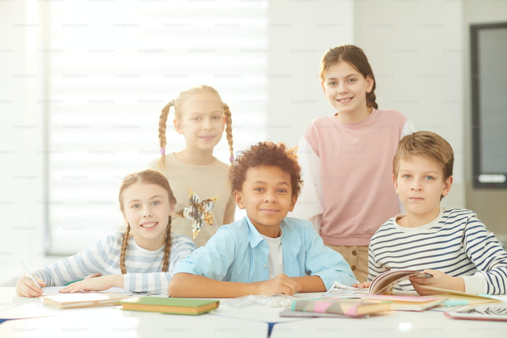 Portrait of smart boys and girls sitting and standing together in modern classroom looking at camera, horizontal shot, copy space