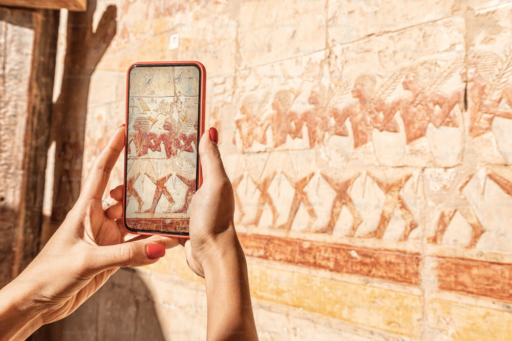 Una bloguera de viajes toma fotos con un teléfono inteligente en los famosos frescos del templo de Hatshepsut en la antigua ciudad de Luxor en Egipto. O usando una guía turística visual