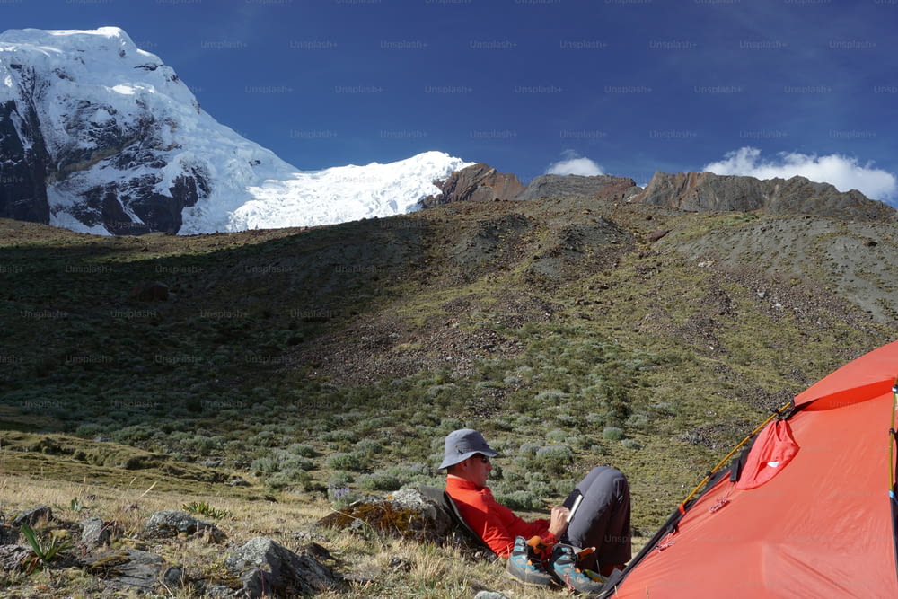 Un alpinista sentado afuera de una tienda de campaña y escribiendo en su diario en la Cordillera Blanca en Perú