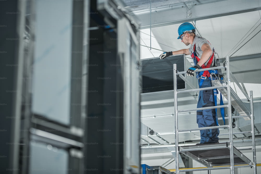Ouvrier de la construction vérifiant le puits de ventilation d’air nouvellement installé au plafond d’un grand bâtiment commercial.