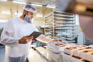 Un ispettore alimentare in una sterile uniforme bianca tiene in mano la tavoletta e guarda i biscotti raccolti. Il controllo degli alimenti è importante se vogliamo cibo sano e di qualità.