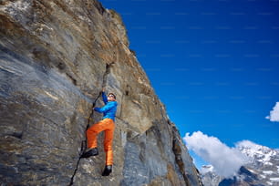 Junger Mann klettert auf eine Felswand, vor blauem Himmel