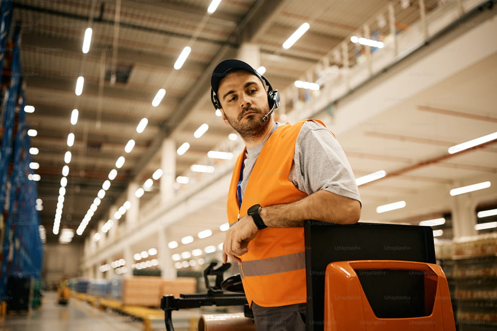 Young worker driving pallet jack while working at industrial warehouse.