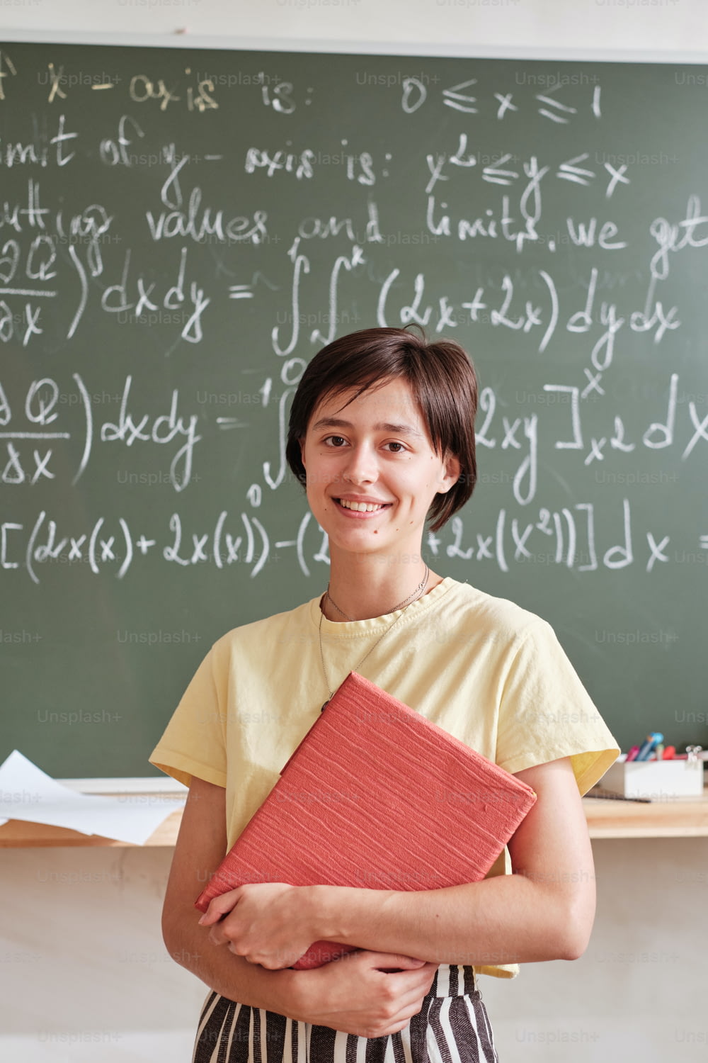 Porträt eines Lehrers mit Büchern, die in die Kamera lächeln, die an der Tafel stehen und an der Universität unterrichten